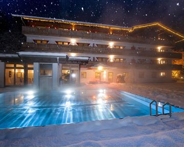 A cozy hotel building in the snow with a illuminated pool. The night sky is clear and starry.