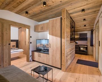 A modern living room with wooden walls and a television. The open kitchen is well equipped and the space feels cozy.