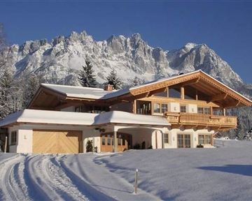 Ein schönes, modernes Chalet im Schnee, umgeben von majestätischen Bergen. Die ruhige Winterlandschaft strahlt Gemütlichkeit aus.