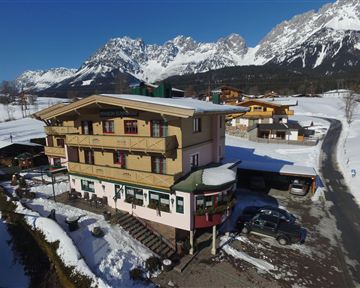 Ein gemütliches Hotel in den Bergen, umgeben von schneebedeckten Landschaften. Die majestätischen Berge erheben sich im Hintergrund unter klarem blauen Himmel.