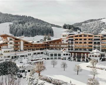 A large, modern hotel in a snowy landscape. In the background, snow-covered mountains and coniferous trees can be seen.
