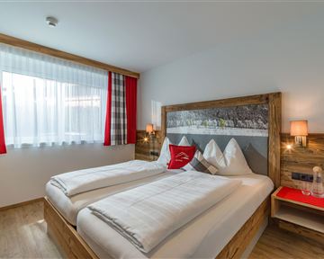 Ein gemütliches Schlafzimmer mit zwei Einzelbetten und stilvollem Holzdesign. Große Fenster lassen viel Tageslicht herein und sorgen für eine angenehme Atmosphäre.