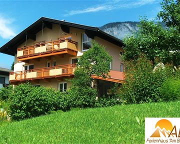 Ein schönes Ferienhaus mit Balkon, umgeben von grünem Gras und Bäumen. Im Hintergrund sind Berge zu sehen.