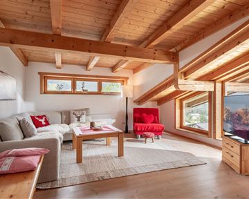 A bright living room with a wooden ceiling and large windows. There are comfortable furniture and a television that complements the space.