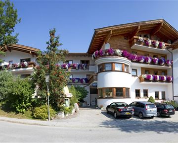 Ein malerisches Hotel mit Balkonen, die mit bunten Blumen dekoriert sind. Umgeben von Bäumen und einem klaren blauen Himmel.