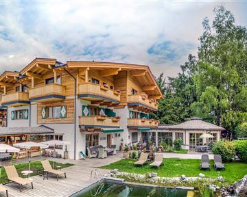 A beautiful hotel in Alpine style with wooden cladding. The garden is green and inviting, with loungers and a swimming pool.
