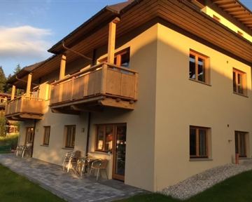 Ein modernes Haus mit Holzbalcon und großen Fenstern. Der Außenbereich ist mit Rasen und Steinen gestaltet.
