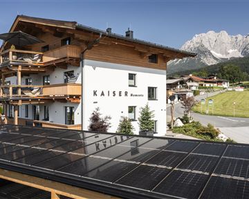Ein modernes Gebäude mit dem Namen "Kaiser" und Balkonen, umgeben von einer wunderschönen Berglandschaft. Solarzellen auf dem Dach ergänzen die nachhaltige Architektur.