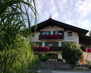 Ein traditionelles Haus mit einem Holzdach und bunten Blumen auf den Balkonen. Die umgebende Vegetation verleiht dem Bild eine einladende Atmosphäre.