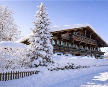 Ein wunderschönes Chalet im Winter mit schneebedecktem Dach und Bäumen. Der klare blaue Himmel verleiht der Szene eine friedliche Atmosphäre.