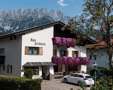 A charming house with colorful flower pots and a picturesque mountain landscape in the background. It is inviting and typical of alpine regions.