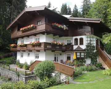 A charming alpine house with balconies and blooming flowers. Surrounded by green countryside and trees.