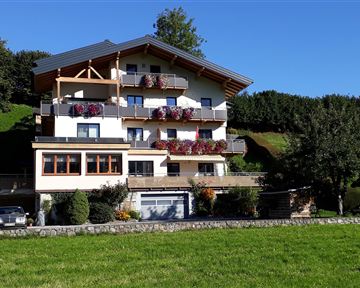 Ein modernes Mehrfamilienhaus mit Balkonen und Blumenschmuck. Im Vordergrund befindet sich eine grüne Wiese.