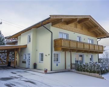 Ein modernes Haus mit einem Holzbalcony in einer verschneiten Umgebung. Der Himmel ist bewölkt, und es ist ruhig und idyllisch.