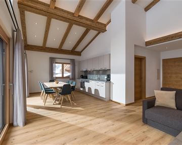 Ein modernes, helles Wohnzimmer mit Holzdecke und großen Fenstern. Es gibt einen Essbereich mit Stühlen und einen gemütlichen Platz zum Entspannen.