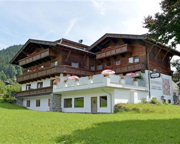 Ein traditionelles Chalet mit Holzbalkonen und roten Blumen. Der grasbewachsene Garten und die umliegenden Berge sorgen für eine malerische Atmosphäre.