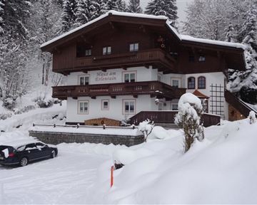 Ein gemütliches Haus im Schnee mit Balkon und Holzverkleidung. Umgeben von verschneiten Bäumen und einer ruhigen Winterlandschaft.