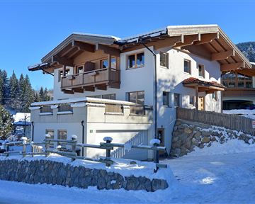 Ein modernes Haus im Schnee, umgeben von Bäumen und einer malerischen Winterlandschaft. Die Architektur verbindet traditionelle und zeitgenössische Elemente.