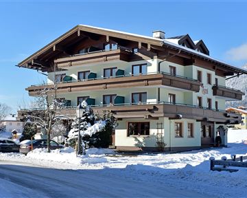 Ein gemütliches Gebäude im alpine Stil, umgeben von Schnee. Die Landschaft ist klar und sonnig, mit einem schönen Blick auf die Berge.