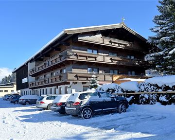 Ein gemütliches Holzgebäude im Schnee mit mehreren Etagen. Vor dem Haus stehen einige Autos auf einem verschneiten Parkplatz.