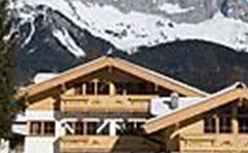 Ein wunderschönes Chalet im Schnee mit beeindruckenden Bergen im Hintergrund. Die klare, blaue Himmel sorgt für eine malerische alpine Kulisse.