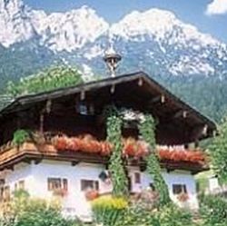 Ein traditionelles Alpenhaus mit blühenden Balkonen. Im Hintergrund erheben sich majestätische Berge unter einem klaren Himmel.