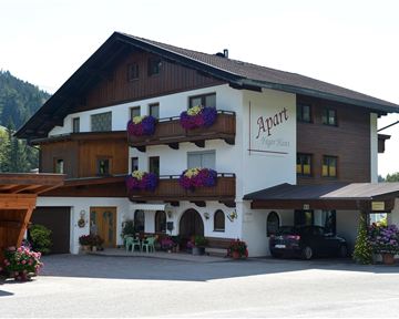 A charming building with several floors and balconies, adorned with flowers. In the background, forests and mountains can be seen.