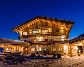 Ein charmantes Holzhaus in den Bergen, beleuchtet von warmem Licht in der Dämmerung. Umgeben von Schnee und einer ruhigen Winterlandschaft.
