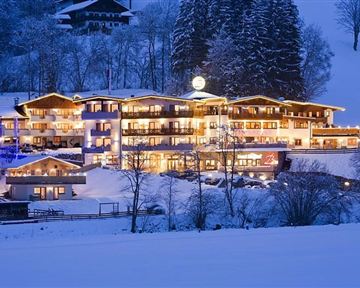 A cozy hotel that glows in the snow at night. Surrounded by snow-covered trees and a wintry landscape.
