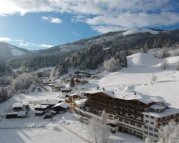 A winter landscape with snow-covered hills and a small village. The buildings are nestled in a quiet, white blanket of snow.