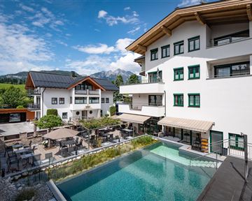 Ein modernes Hotel mit einem schönen Außenbereich und einem Pool. Im Hintergrund sind grüne Wiesen und Berge zu sehen.