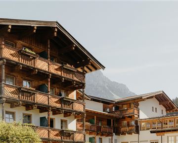 A charming building in alpine style with balconies and wooden cladding. In the background, mountains can be seen, providing a picturesque landscape.