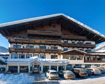 A cozy hotel in a snowy landscape. The façade is designed in traditional Alpine style and is surrounded by snow-covered mountains.