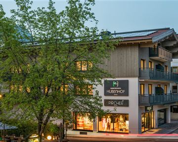 Ein modernes Gebäude mit einem schönen Holzdesign und großen Fenstern. Bäume umgeben das Haus und beleuchten die Umgebung sanft.