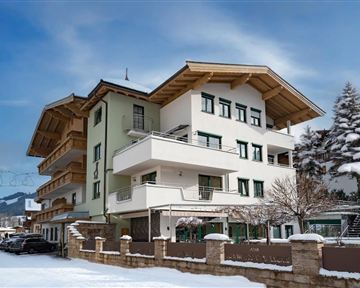 A modern building in alpine style, surrounded by snow and a clear sky. In the foreground, a quiet road with some vehicles can be seen.