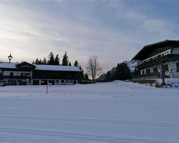 Ein malerischer Wintertag mit schneebedeckten Gebäuden und Bäumen. Die sanfte Abenddämmerung schafft eine ruhige Atmosphäre.