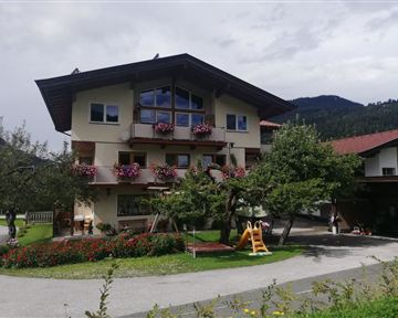 A charming building with blooming balcony boxes. In the foreground, flowerbeds and a playground can be seen.