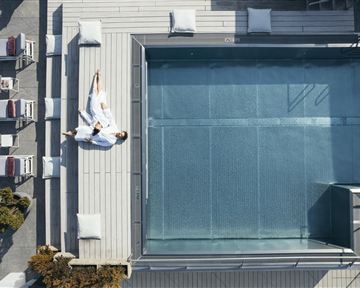 Ein moderner Pool mit Liegen auf einer Terrasse. Eine Person entspannt sich in einem Bademantel neben dem Wasser.