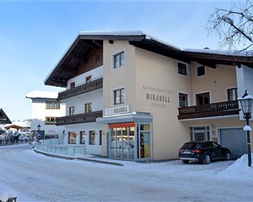 Ein gemütliches Gebäude im Schnee, das als Pension dient. Die Umgebung ist winterlich mit schneebedeckten Straßen und Bäumen.