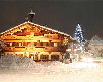 Ein charmantes Holzhaus im Winter mit warmem Licht. Der schneebedeckte Boden und ein beleuchteter Weihnachtsbaum schaffen eine festliche Atmosphäre.