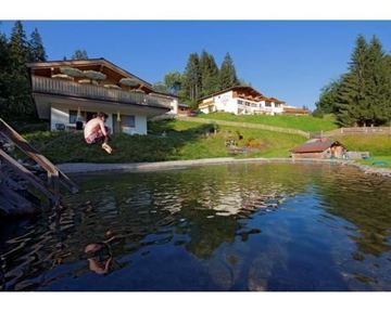 A peaceful pond surrounded by trees and beautiful scenery. In the background, several buildings can be seen, ideal for a relaxing stay.