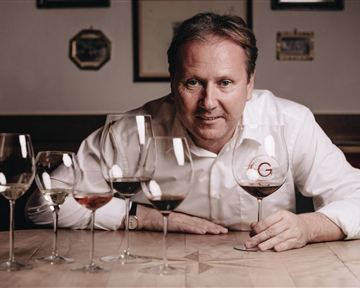 A man is sitting at a table with several wine glasses. He is holding a glass of wine in his hand and smiling.