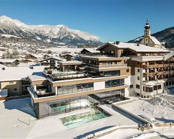 A modern hotel in a snowy landscape with mountain views. The building has large windows and an outdoor pool.