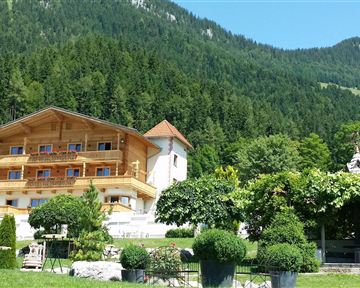Ein gemütliches Holzhaus inmitten einer grünen Berglandschaft. Der Himmel ist klar und die Umgebung ist üppig bewachsen.