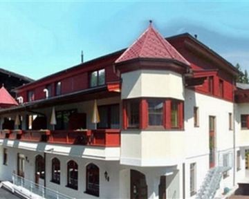 Ein charmantes Gebäude im alpinen Stil mit roten und weißen Elementen. Die Fassade hat viele Fenster und einen attraktiven Balkon.