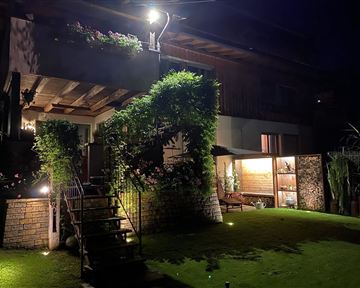 Ein schön beleuchtetes Haus mit einem begrünten Garten. Die Pflanzen und Lichter sorgen für eine gemütliche Atmosphäre in der Nacht.