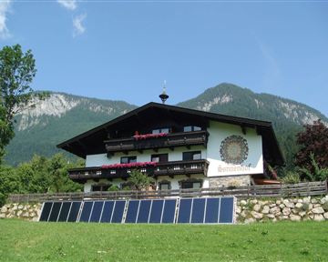 Ein gemütliches, traditionelles Bauernhaus in den Bergen. Solarzellen sind im Vordergrund aufgestellt, um umweltfreundliche Energie zu nutzen.