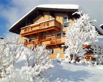 Ein charmantes Haus im Schnee mit Holzverzierungen und Balkonen. Die Umgebung ist von weißem Schnee und schneebedeckten Bäumen geprägt.