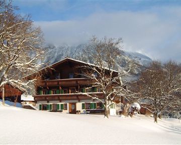 Ein schönes Chalet in der verschneiten Landschaft. Im Hintergrund sind Berge und Bäume zu sehen.