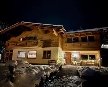 Ein gemütliches Holzhaus im Schnee bei Nacht. Die Fassade ist warm beleuchtet und schafft eine einladende Atmosphäre.